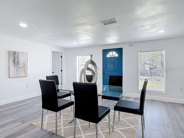 dining space with baseboards, a textured ceiling, visible vents, and wood finished floors