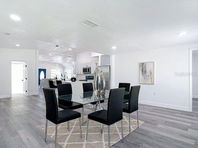 dining space with light wood finished floors, baseboards, visible vents, and a textured ceiling