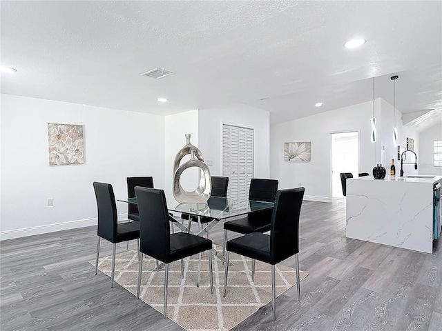 dining area featuring a textured ceiling, wood finished floors, visible vents, baseboards, and vaulted ceiling