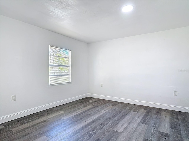 spare room with baseboards and dark wood-style flooring