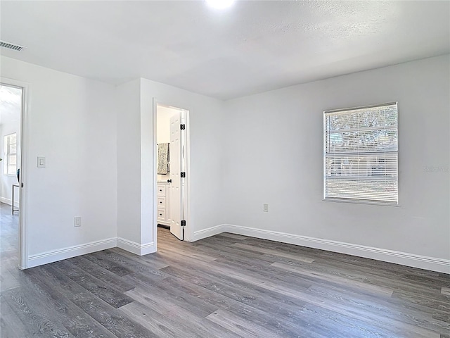 unfurnished room with dark wood-style flooring, visible vents, and baseboards