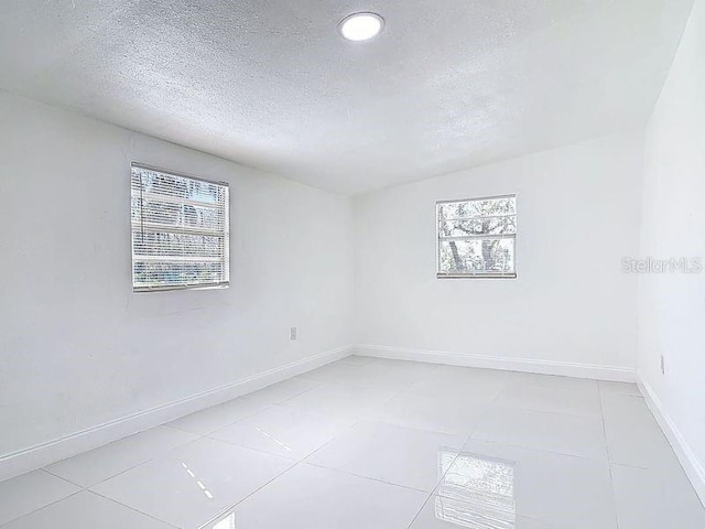 unfurnished room featuring a textured ceiling, light tile patterned floors, a wealth of natural light, and baseboards