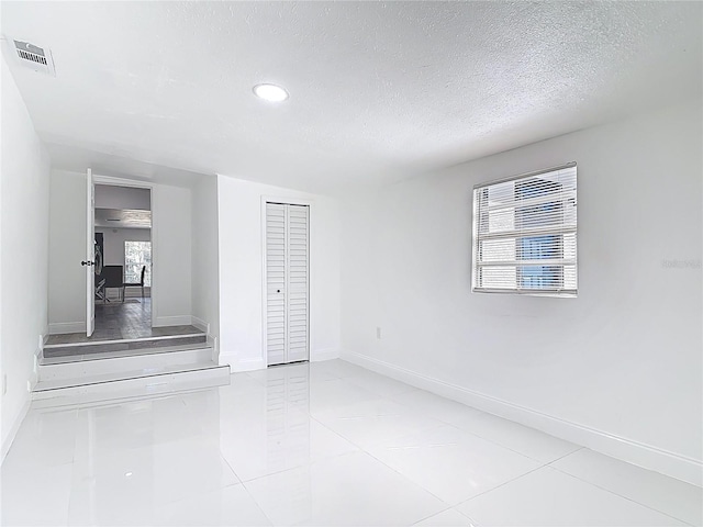 empty room with a textured ceiling, tile patterned flooring, visible vents, and baseboards