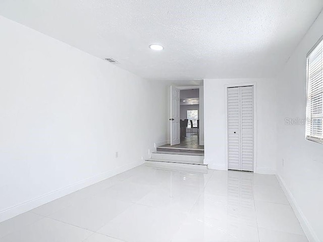 spare room featuring visible vents, a textured ceiling, and baseboards