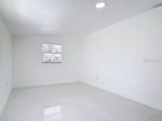 empty room featuring light tile patterned floors, baseboards, visible vents, and a textured ceiling