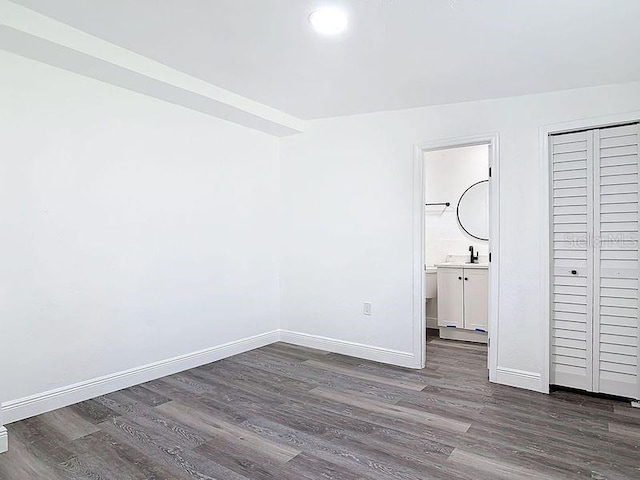 unfurnished bedroom with a sink, a closet, baseboards, and dark wood-style flooring