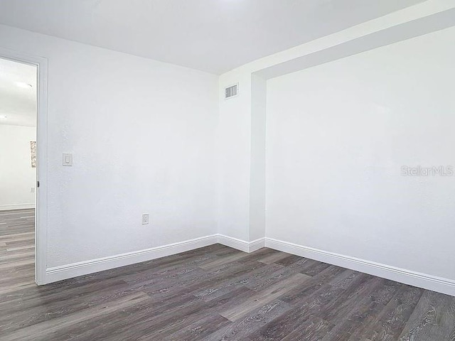 spare room featuring dark wood-style flooring, visible vents, and baseboards