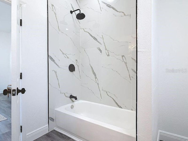 full bathroom featuring washtub / shower combination, baseboards, wood finished floors, and a textured wall