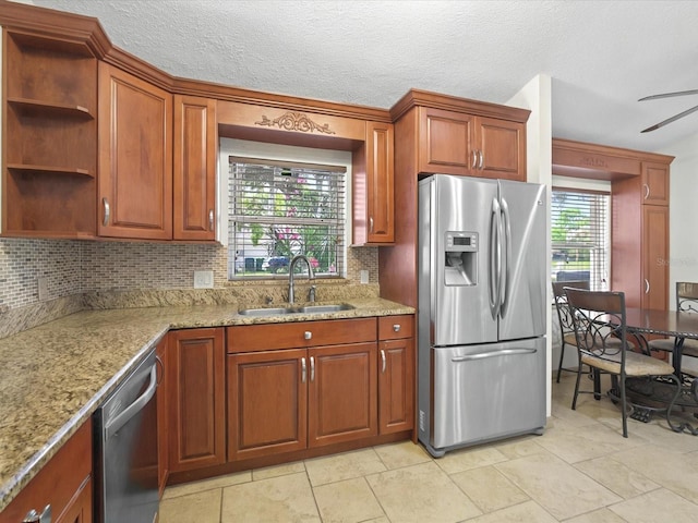 kitchen with backsplash, light stone countertops, stainless steel appliances, a ceiling fan, and a sink