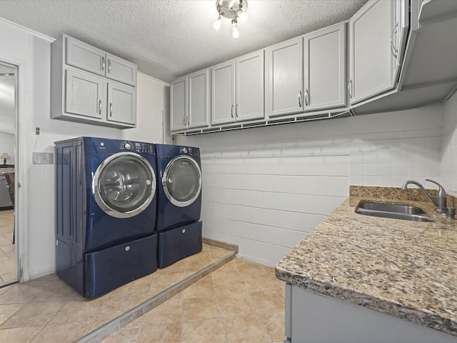 laundry room featuring light tile patterned floors, cabinet space, a sink, a textured ceiling, and washer and dryer