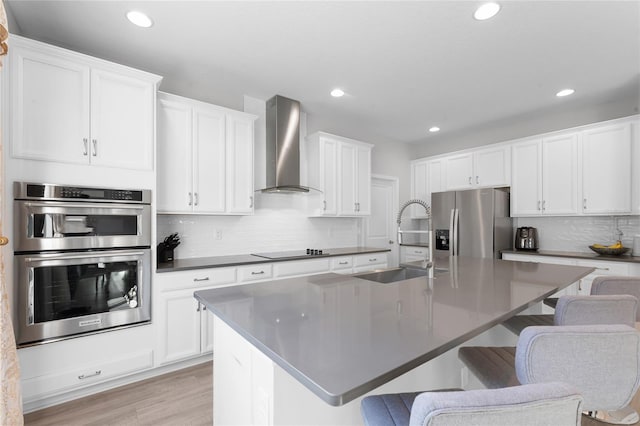 kitchen featuring a sink, appliances with stainless steel finishes, a breakfast bar area, and wall chimney range hood