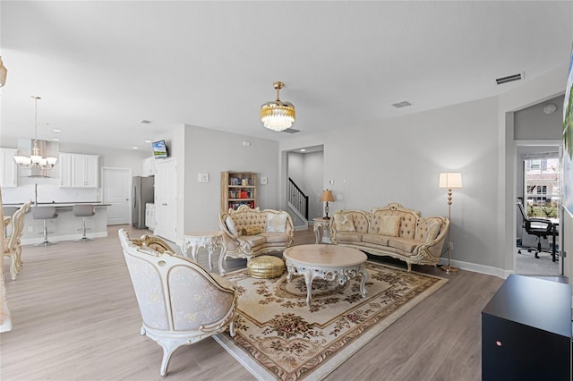 living room with stairway, light wood-type flooring, visible vents, and a chandelier