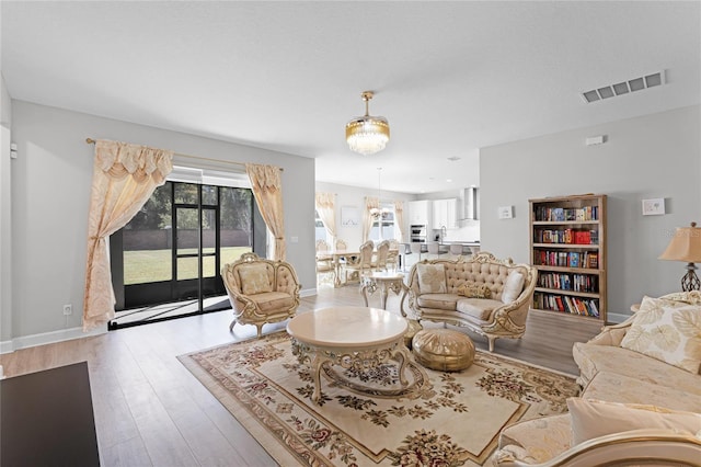 living area with visible vents, baseboards, a notable chandelier, and wood finished floors