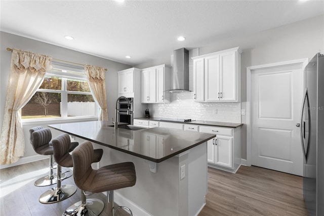 kitchen with appliances with stainless steel finishes, a kitchen bar, dark countertops, wall chimney exhaust hood, and backsplash