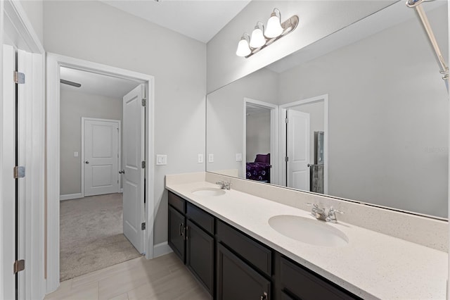 ensuite bathroom featuring a sink, connected bathroom, baseboards, and double vanity