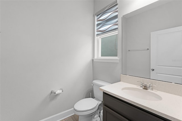 half bath with vanity, toilet, wood finished floors, and baseboards