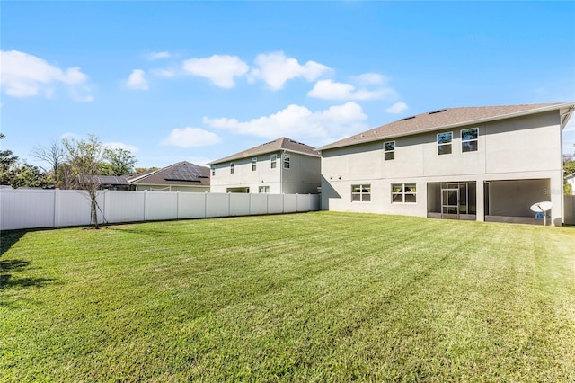 rear view of house with a yard, fence, and stucco siding