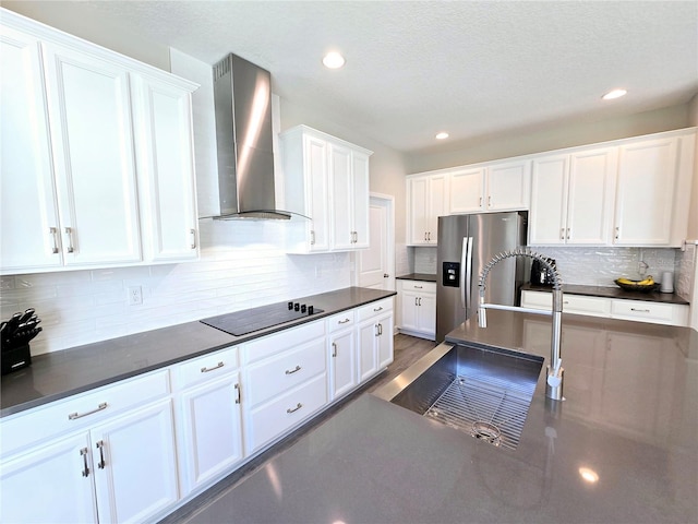 kitchen featuring dark countertops, white cabinetry, stainless steel fridge, wall chimney range hood, and black electric stovetop