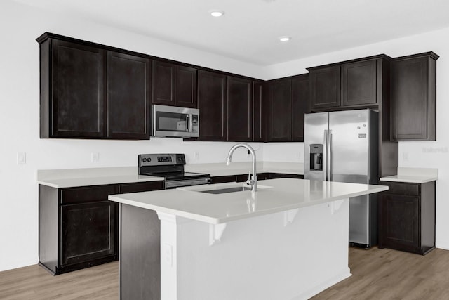 kitchen featuring a kitchen island with sink, a sink, stainless steel appliances, light wood-style floors, and light countertops