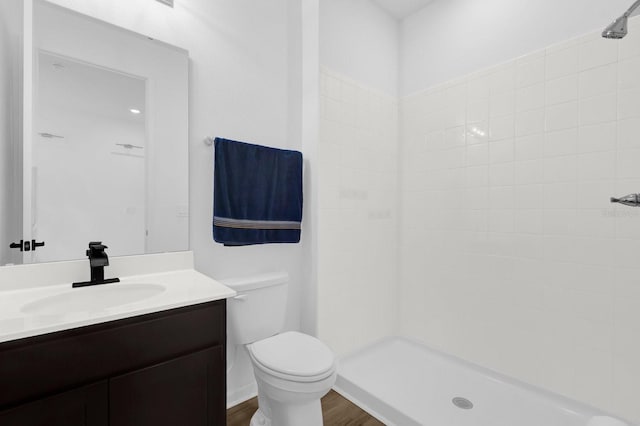 bathroom featuring tiled shower, toilet, vanity, and wood finished floors