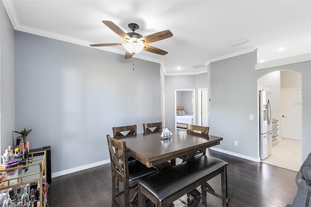 dining room with baseboards, arched walkways, wood finished floors, and crown molding