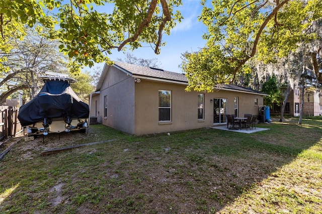 rear view of house with stucco siding, a patio, a lawn, and fence