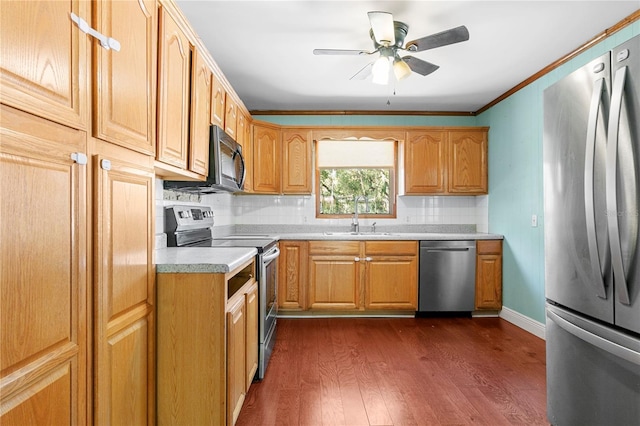 kitchen with a sink, dark wood finished floors, appliances with stainless steel finishes, crown molding, and light countertops