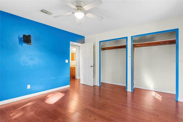 unfurnished bedroom featuring visible vents, two closets, ceiling fan, baseboards, and wood finished floors