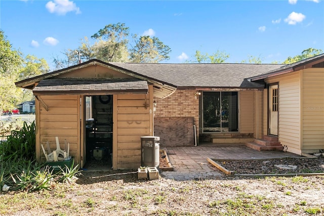 back of property with entry steps, a patio, brick siding, and a shingled roof