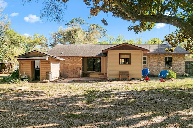 rear view of house featuring brick siding, fence, an outbuilding, a storage unit, and a patio