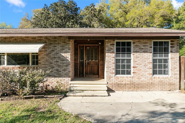 view of exterior entry with brick siding and a shingled roof