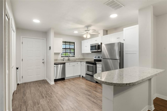 kitchen with light wood-type flooring, visible vents, appliances with stainless steel finishes, white cabinets, and light stone countertops