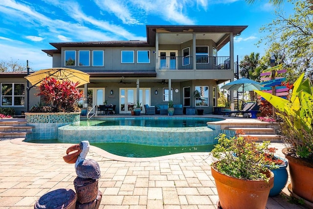 rear view of property with a patio, a balcony, ceiling fan, french doors, and an infinity pool