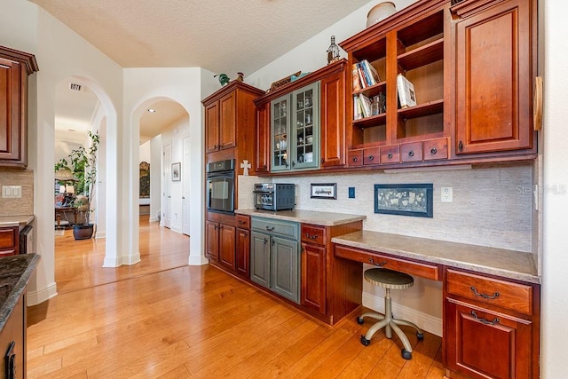 kitchen with black oven, a toaster, light wood-style floors, and arched walkways