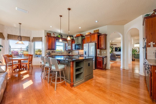 kitchen with arched walkways, light wood-style floors, a center island, and stainless steel refrigerator with ice dispenser