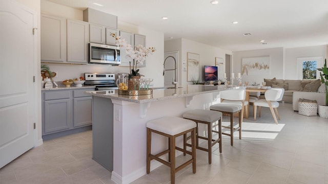 kitchen with a breakfast bar, stainless steel appliances, gray cabinetry, open floor plan, and a sink