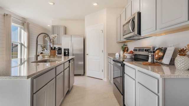 kitchen with a center island with sink, stainless steel appliances, gray cabinetry, a sink, and recessed lighting