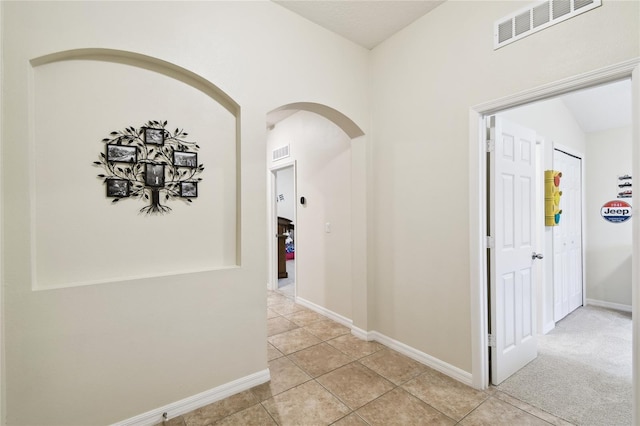 hall with light colored carpet, light tile patterned flooring, baseboards, and visible vents