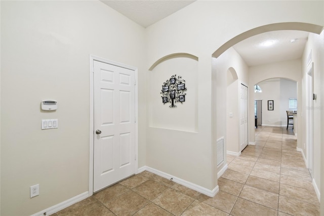 corridor featuring light tile patterned floors, visible vents, baseboards, and arched walkways