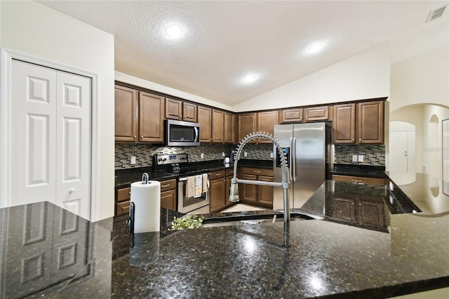 kitchen with visible vents, vaulted ceiling, appliances with stainless steel finishes, arched walkways, and a sink