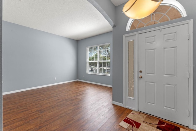 foyer with arched walkways, a textured ceiling, baseboards, and dark wood-style flooring