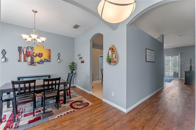 dining room with hardwood / wood-style floors, visible vents, baseboards, an inviting chandelier, and arched walkways