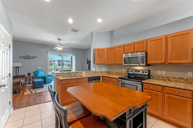 kitchen with open floor plan, appliances with stainless steel finishes, a peninsula, light tile patterned flooring, and a sink