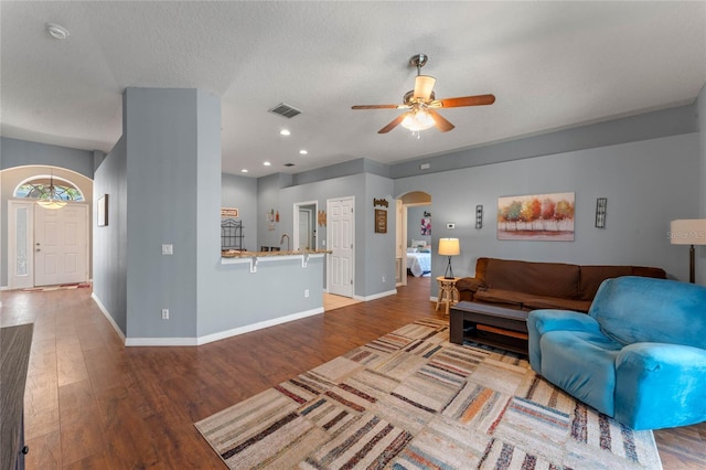 living area with visible vents, baseboards, wood finished floors, arched walkways, and a ceiling fan