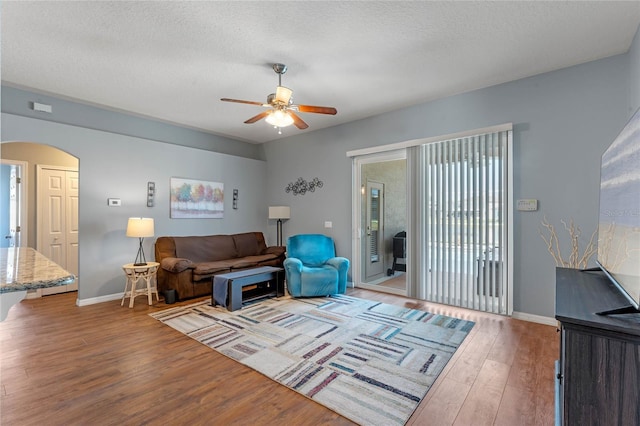 living room featuring baseboards, wood finished floors, arched walkways, a textured ceiling, and a ceiling fan