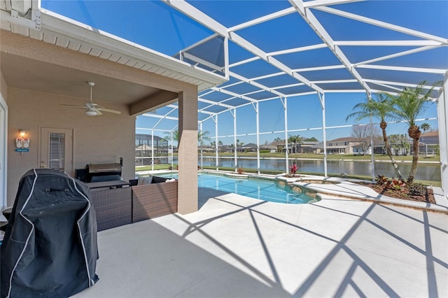 outdoor pool with grilling area, a water view, glass enclosure, a patio, and a ceiling fan