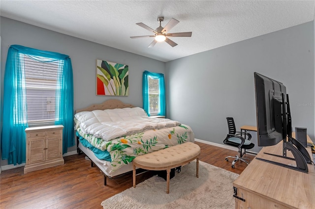 bedroom with a textured ceiling, a ceiling fan, baseboards, and wood finished floors