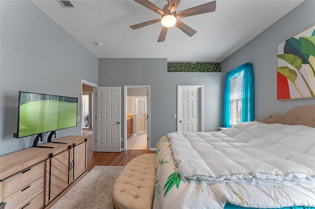 bedroom featuring a ceiling fan, wood finished floors, visible vents, a textured ceiling, and connected bathroom