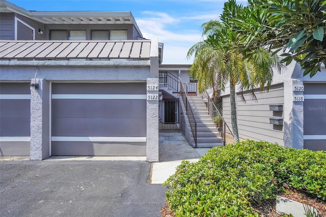 townhome / multi-family property with stairway, metal roof, a garage, driveway, and a standing seam roof