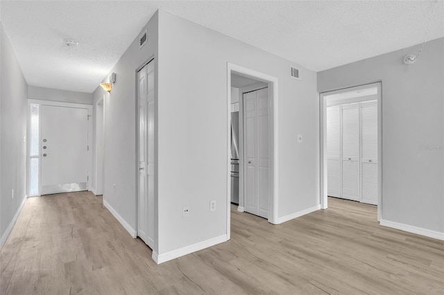 hallway with light wood finished floors, visible vents, a textured ceiling, and baseboards